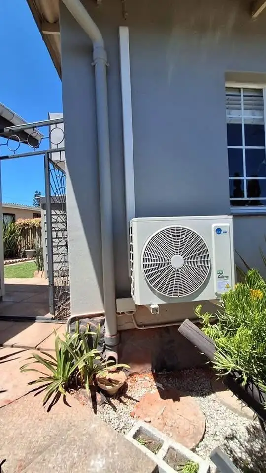 Aircon outdoor unit installed at ground level against a grey wall with tidy pipe cover